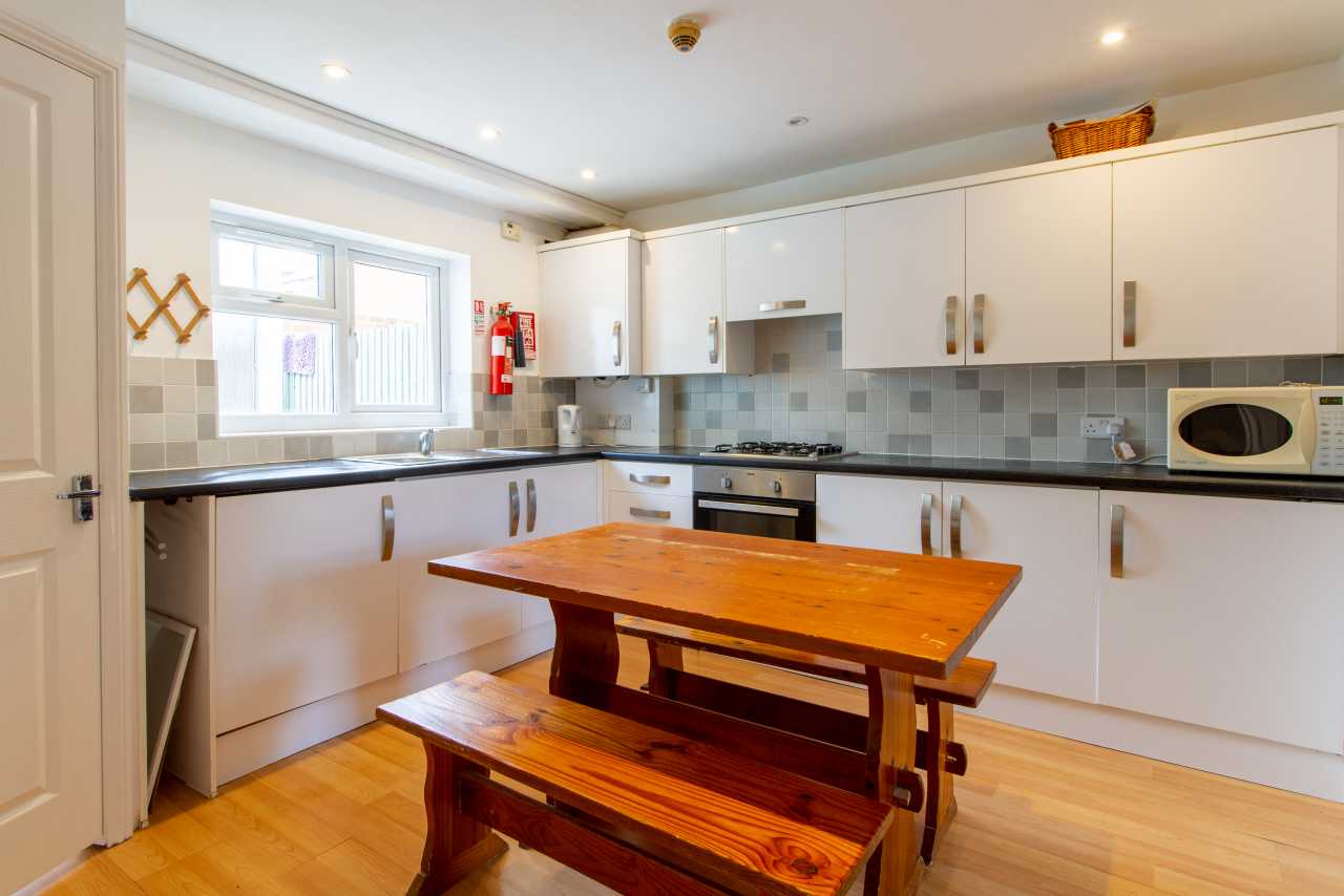 Bright fitted kitchen with white cabinets, tiled backsplash, appliances, and a wooden dining table with benches.