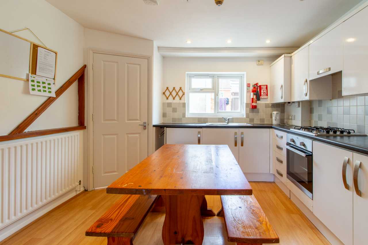 Kitchen with white cabinets, tiled backsplash, cooker, sink, wooden table and benches.