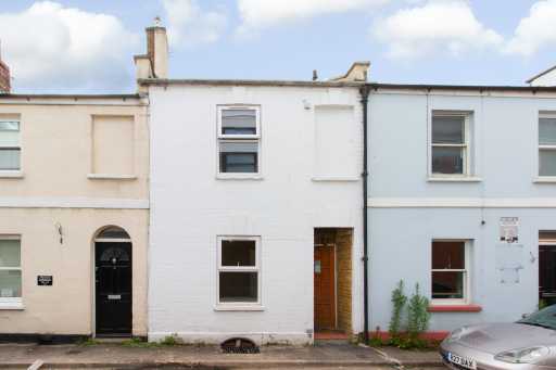 Street-facing view of attached terraced houses with doors, windows, chimneys and a parked car.
