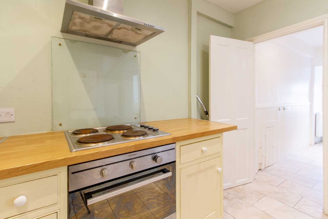 Bright fitted kitchen with an electric hob, oven, extractor hood, wooden worktops and an open doorway.
