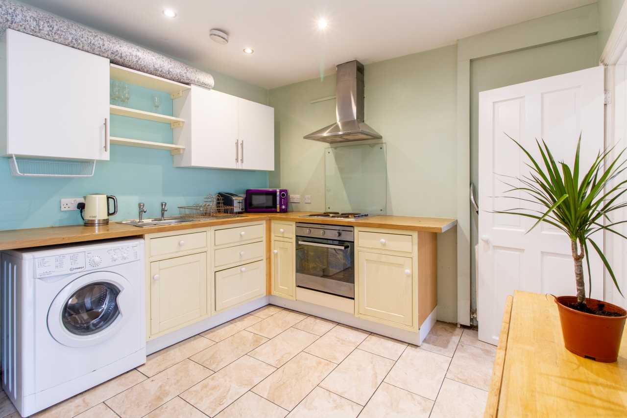 Bright fitted kitchen with cream cabinets, wooden countertops, a washing machine, oven, hob and potted plant.
