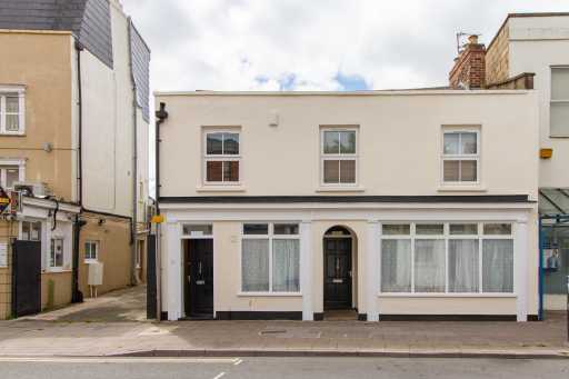 Front exterior of a two-storey terraced residential building with windows, doors and pavement.