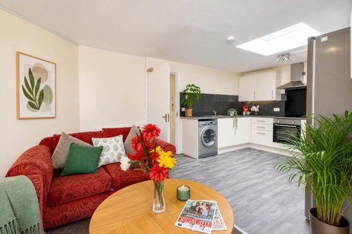 Open-plan living area with a red sofa, coffee table, fitted kitchen, skylight and potted plants.
