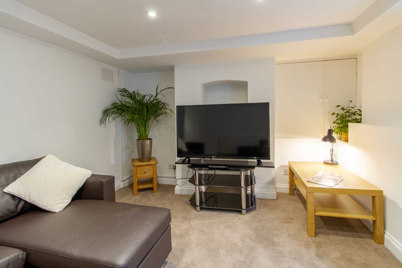 Furnished living room with a sofa, television, plants and a wooden table.