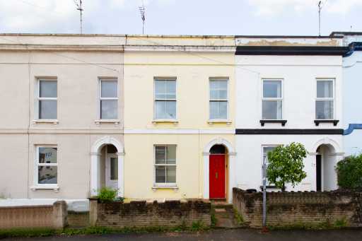 A row of attached terraced houses with painted facades, windows, front doors, low walls and small front gardens.