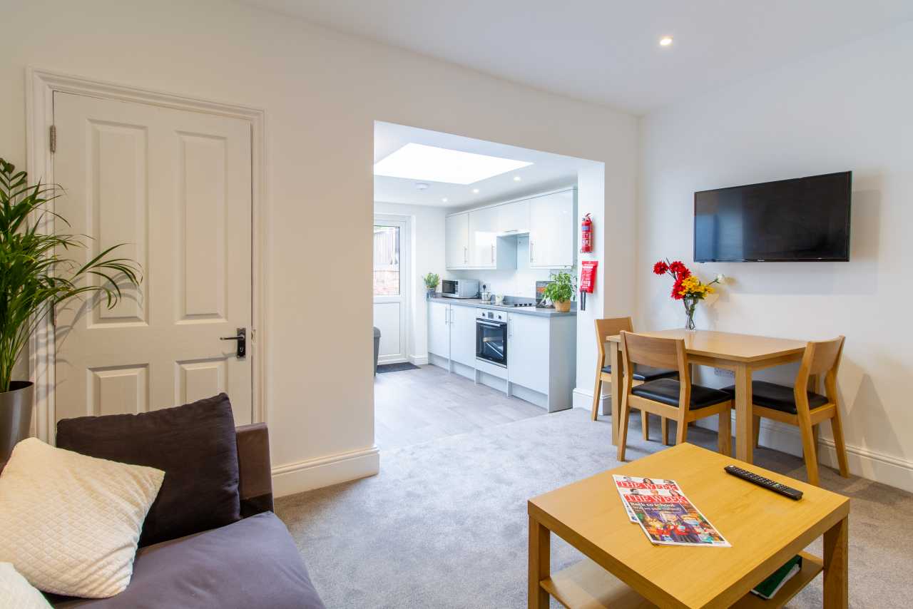 Bright shared living and dining area with a sofa, television, dining table, coffee table and open kitchen.