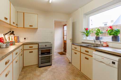 A bright residential kitchen with cream cabinets, a cooker, sink, dishwasher and window.