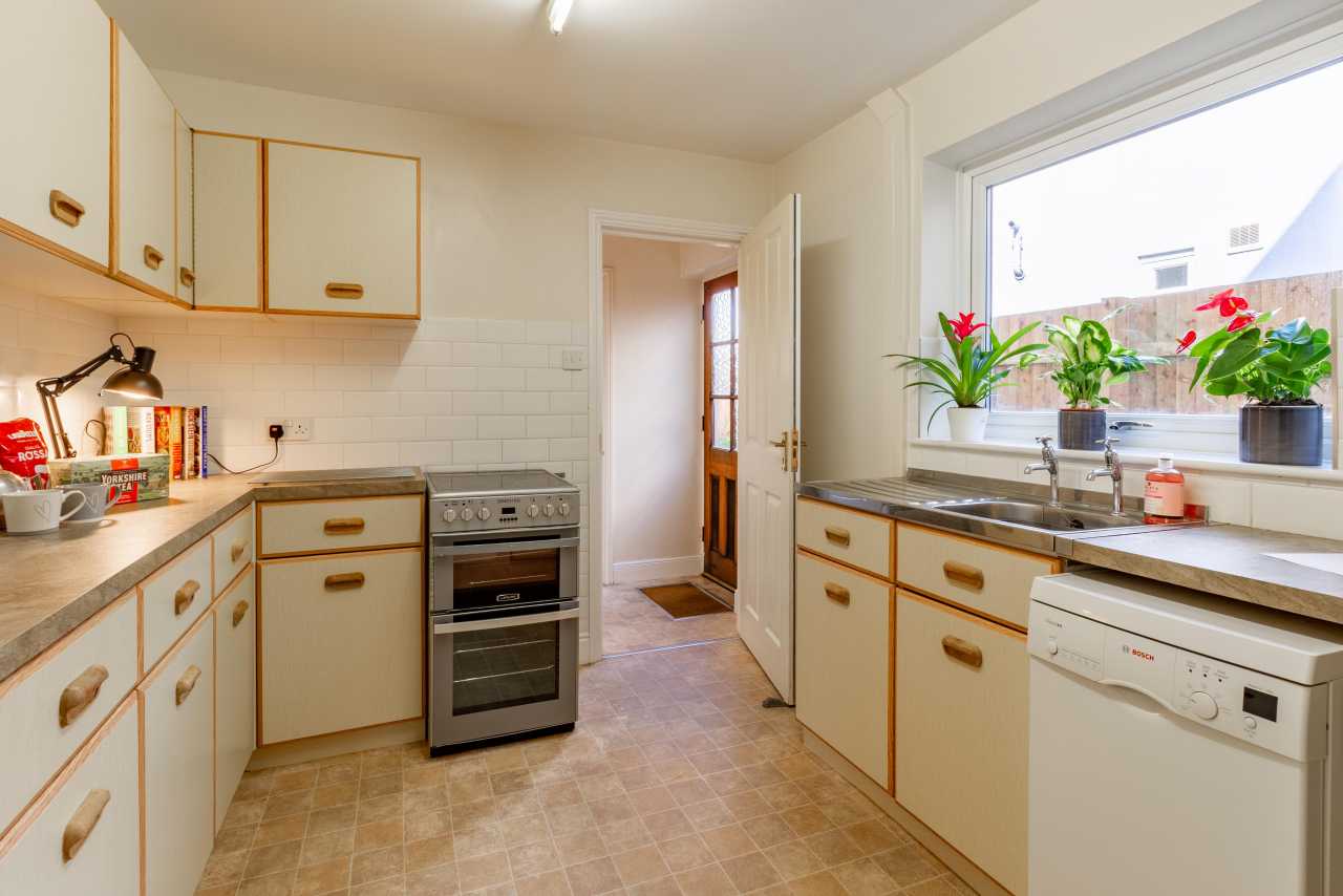 A bright residential kitchen with cream cabinets, a cooker, sink, dishwasher and window.