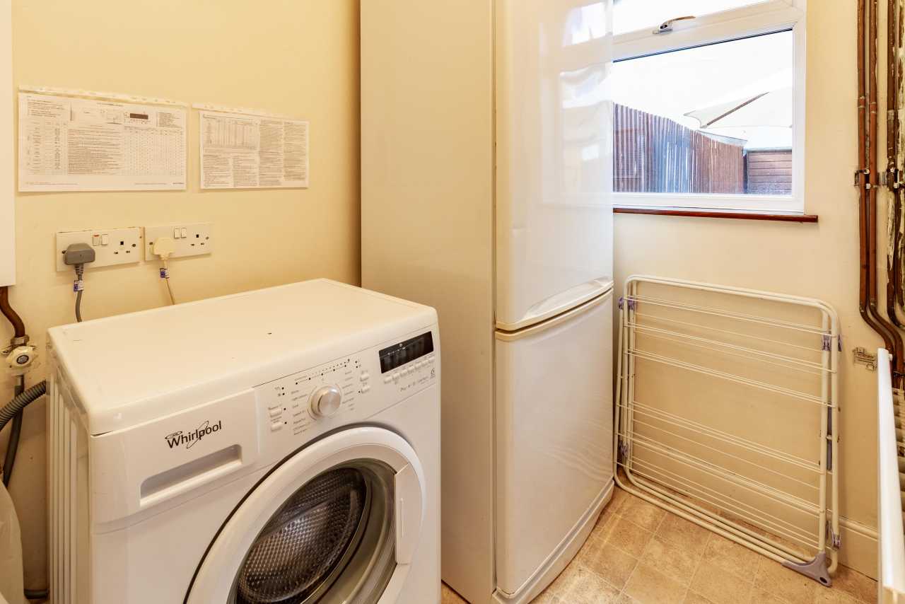 Utility room with a washing machine, tall freezer, window and folding drying rack.
