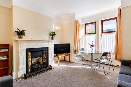 Furnished communal sitting room with an ornate fireplace, television, seating, table and large bay windows.
