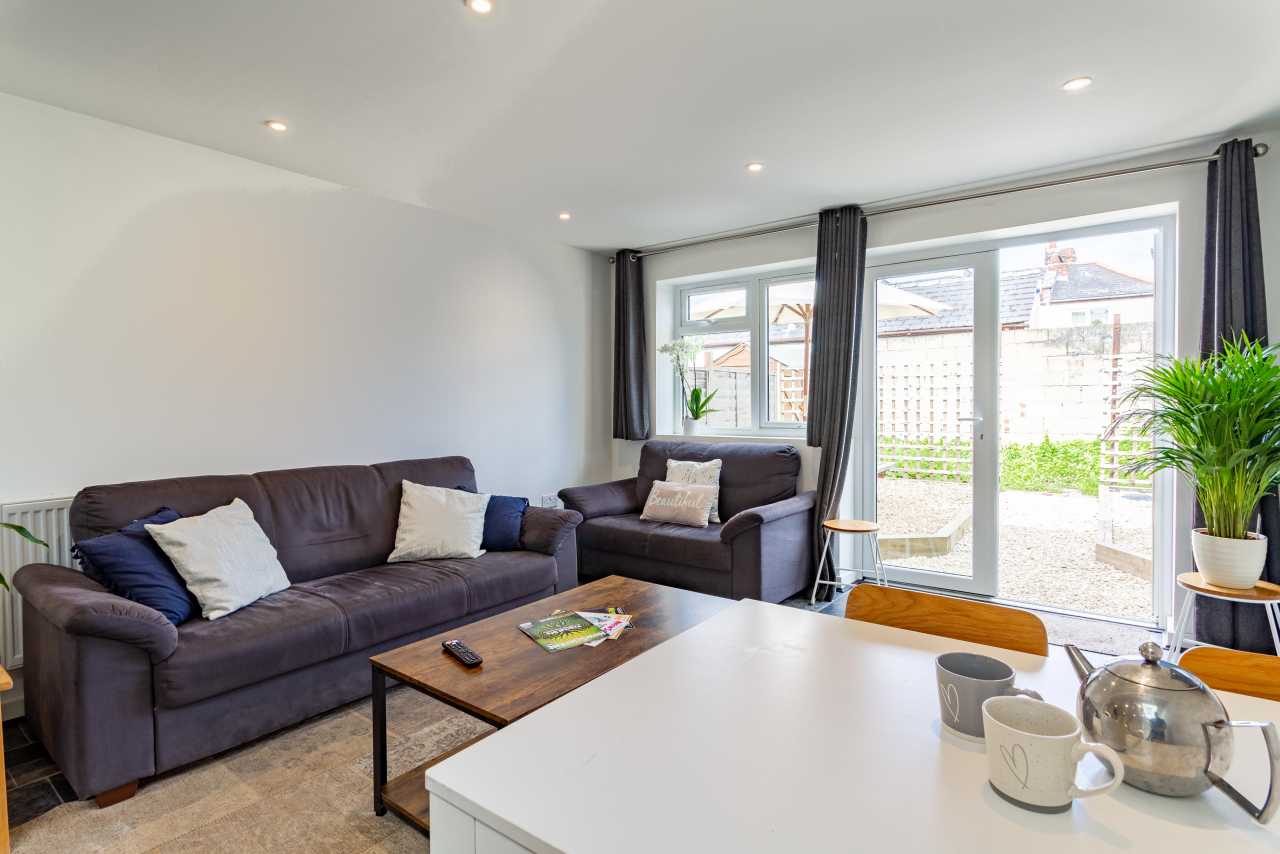 Open-plan living area with two sofas, a coffee table, dining table, large windows and a glass door leading to a patio.
