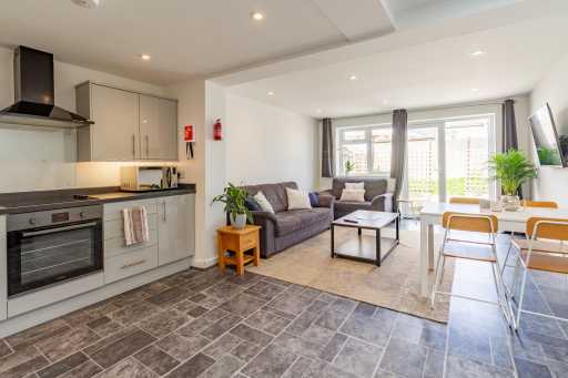 Open-plan kitchen and living area with a dining table, sofa, television and large windows.