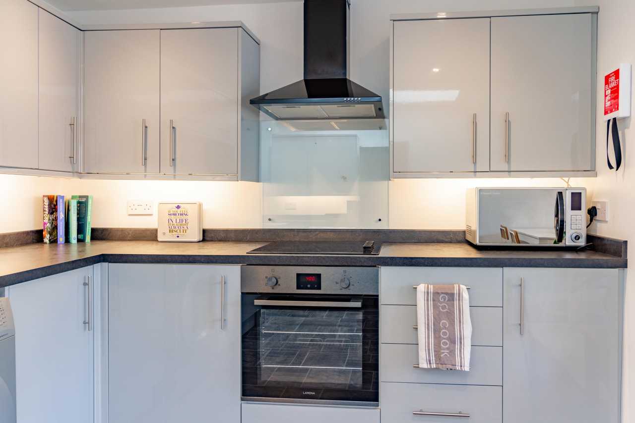 A modern fitted kitchen with white cabinets, a black countertop, hob, oven, extractor hood, microwave and sink.