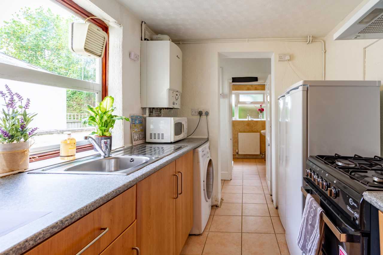 A bright residential kitchen with cabinets, sink, microwave, washing machine, refrigerator and gas cooker.
