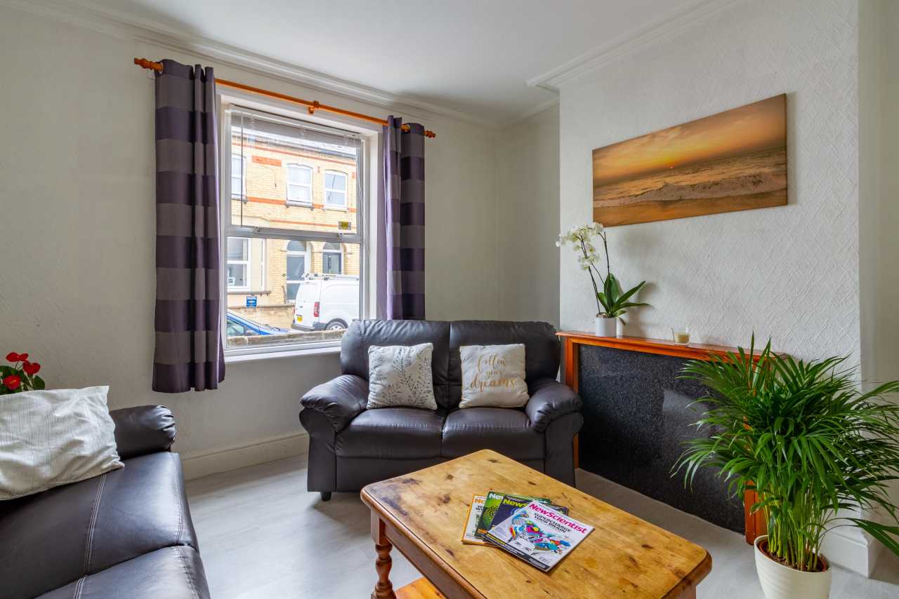 Bright sitting room with sofas, a wooden coffee table, curtains, plants and a fireplace.