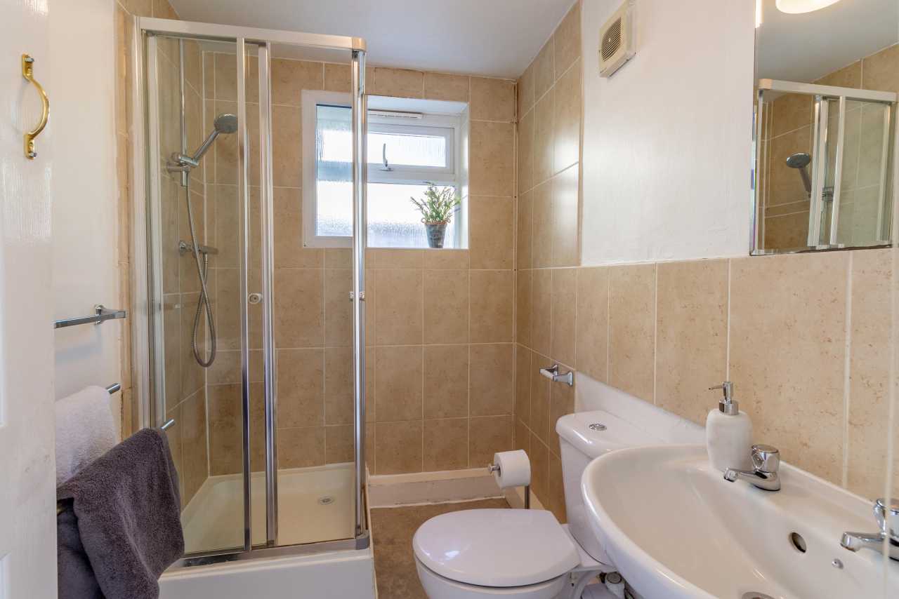 A tiled bathroom with a glass shower enclosure, toilet, sink, mirror and window.