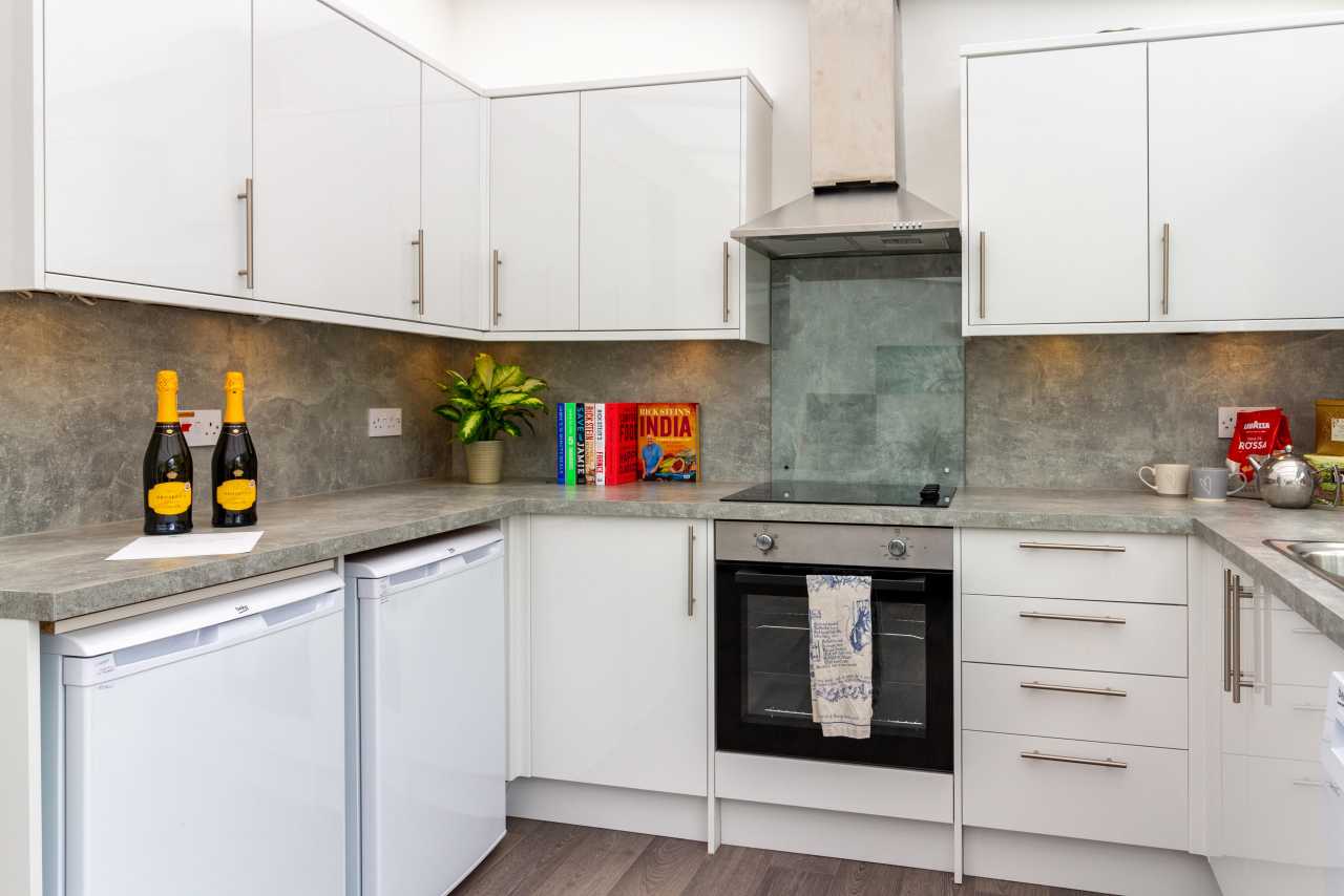 Bright modern white kitchen with fitted cabinets, grey worktops, oven, extractor hood and breakfast items.