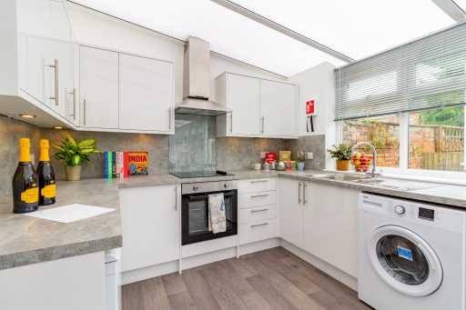 Bright modern kitchen with white cabinets, oven, washing machine, countertops and a large window.