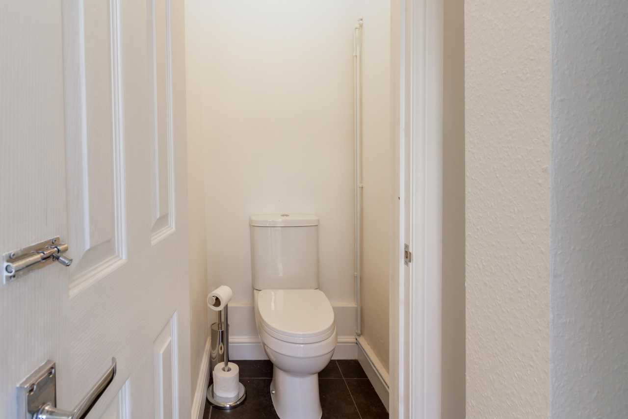 A small toilet room with a toilet, toilet paper holder, brush, and dark tiled floor.