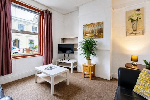 Furnished living room with a sofa, coffee table, television, plants, artwork and a large window.