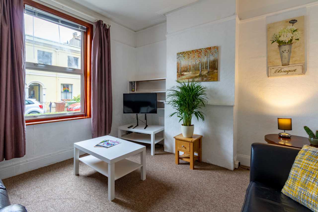 Furnished living room with a sofa, coffee table, television, plants, artwork and a large window.