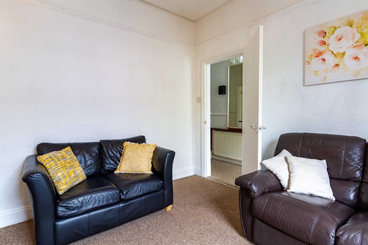 A furnished sitting room with two leather sofas, cushions, carpet and floral wall art.