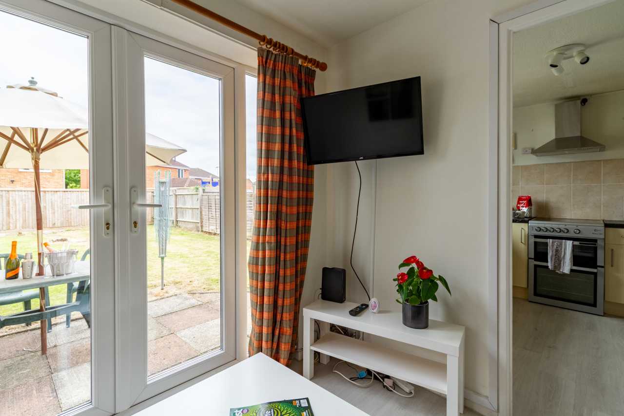 Bright living area with patio doors, a wall-mounted television, a small console table, and an adjoining kitchen.
