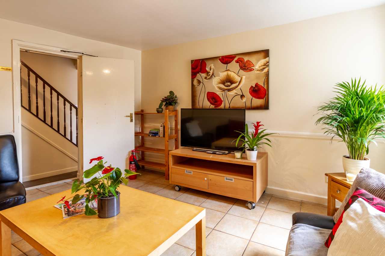 Shared living room with seating, a television, plants, wall art, and a staircase.