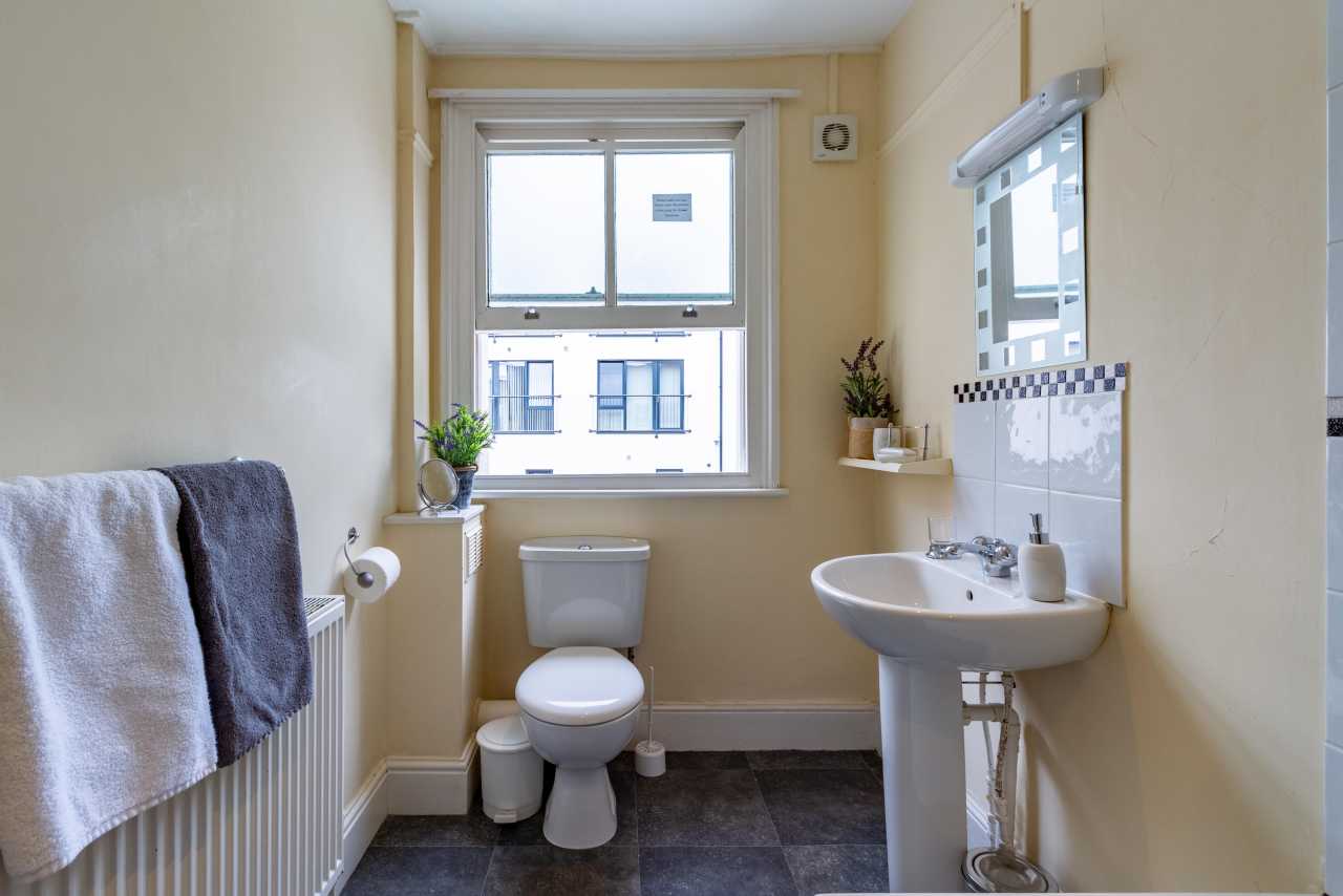 A small bathroom with a toilet, pedestal sink, radiator, window and tiled splashback.
