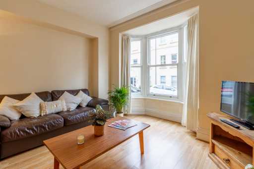 Bright living room with a brown sofa, coffee table, television, plants and a bay window.