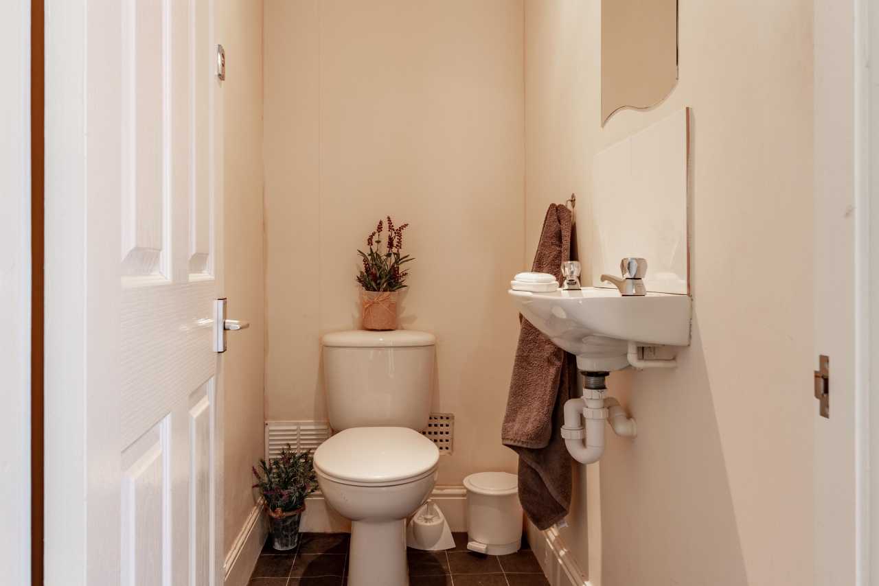 A small toilet room with a toilet, wall-mounted sink, mirror, plants and tiled floor.