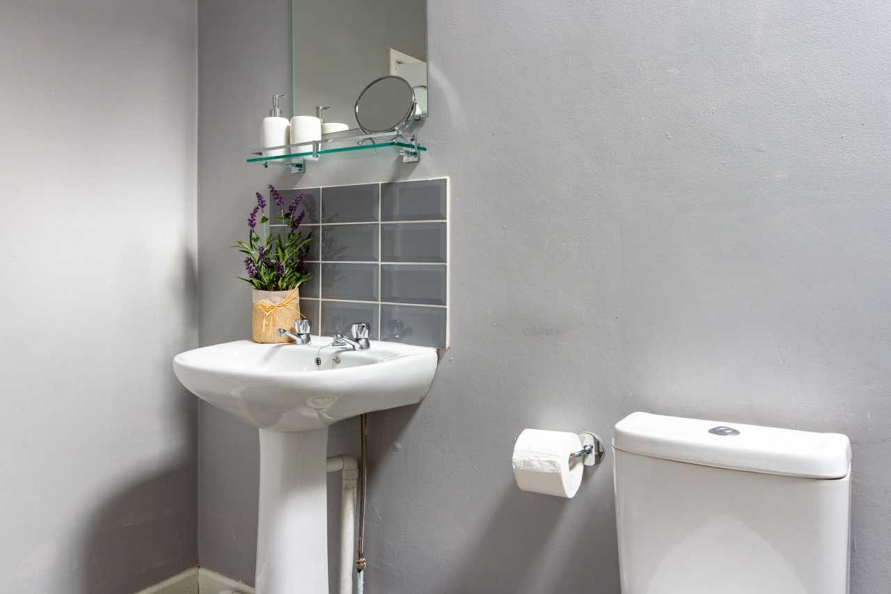 A small bathroom with a pedestal sink, wall mirror, tiled backsplash, toilet and toilet roll holder.