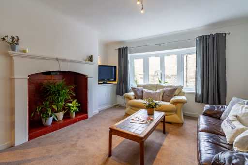 Bright living room with a fireplace, seating, coffee table, television and large bay window.