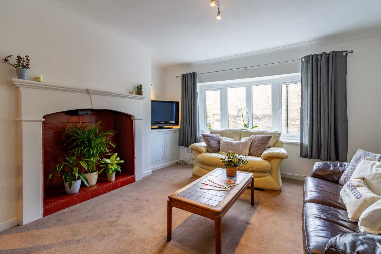 Bright living room with a fireplace, seating, coffee table, television and large bay window.