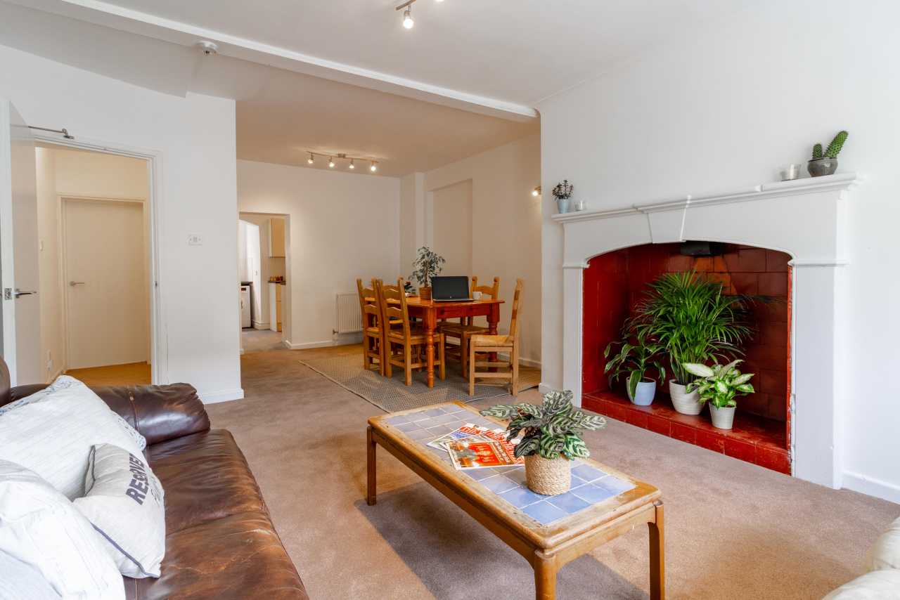 Open-plan living and dining area with sofas, a wooden dining table, and a large white fireplace containing potted plants.