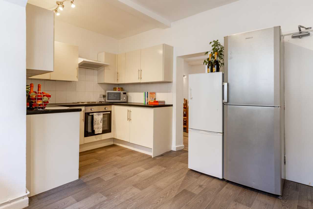 A fitted kitchen with white cabinets, an oven, microwave, sink, and large refrigerator-freezer.