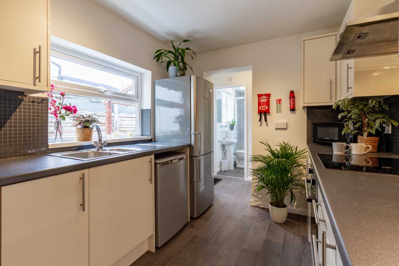 A bright fitted kitchen with cabinets, sink, dishwasher, refrigerator, oven and countertop appliances.