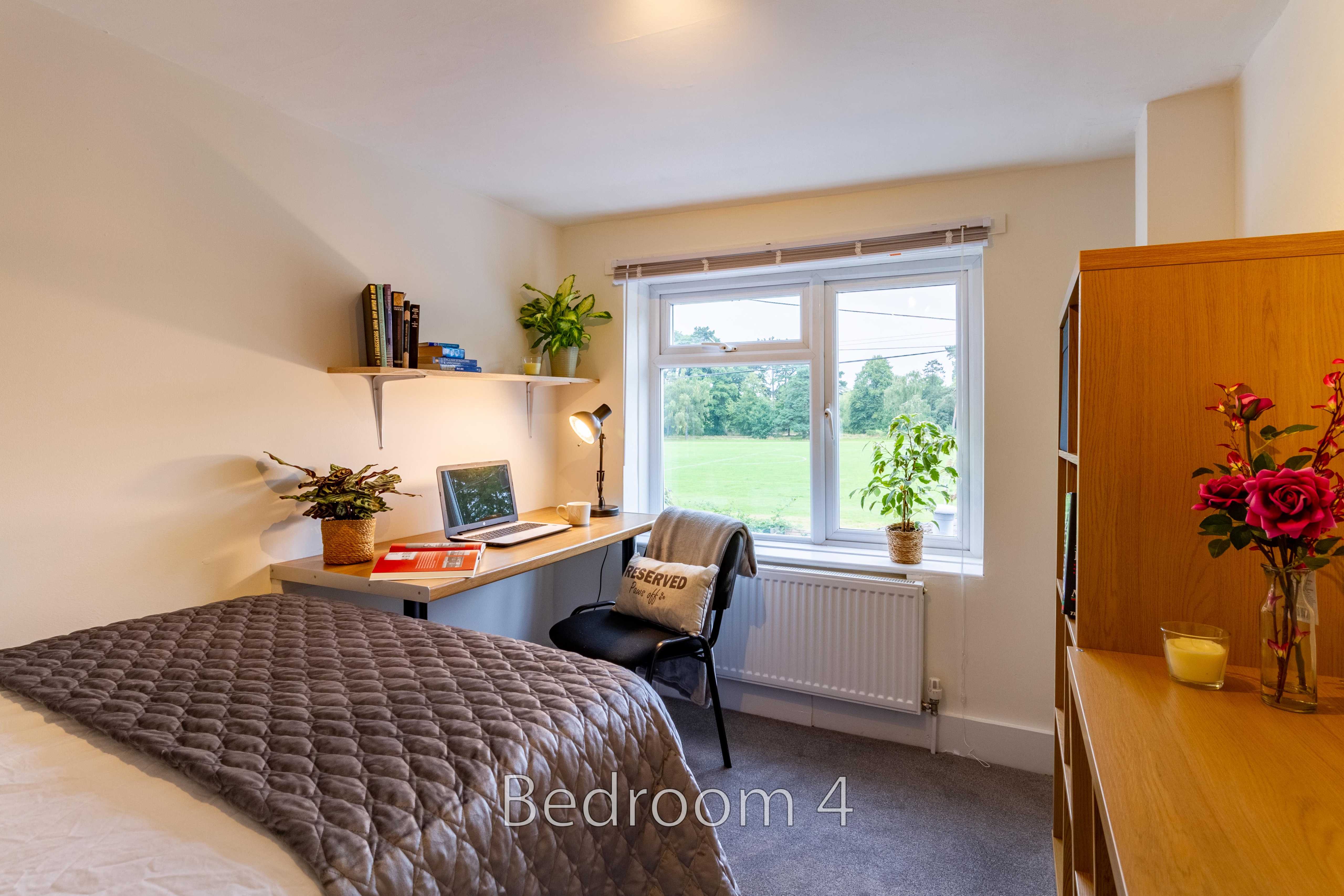 A furnished bedroom with a double bed, desk, chair, window, radiator, shelving and wooden furniture.