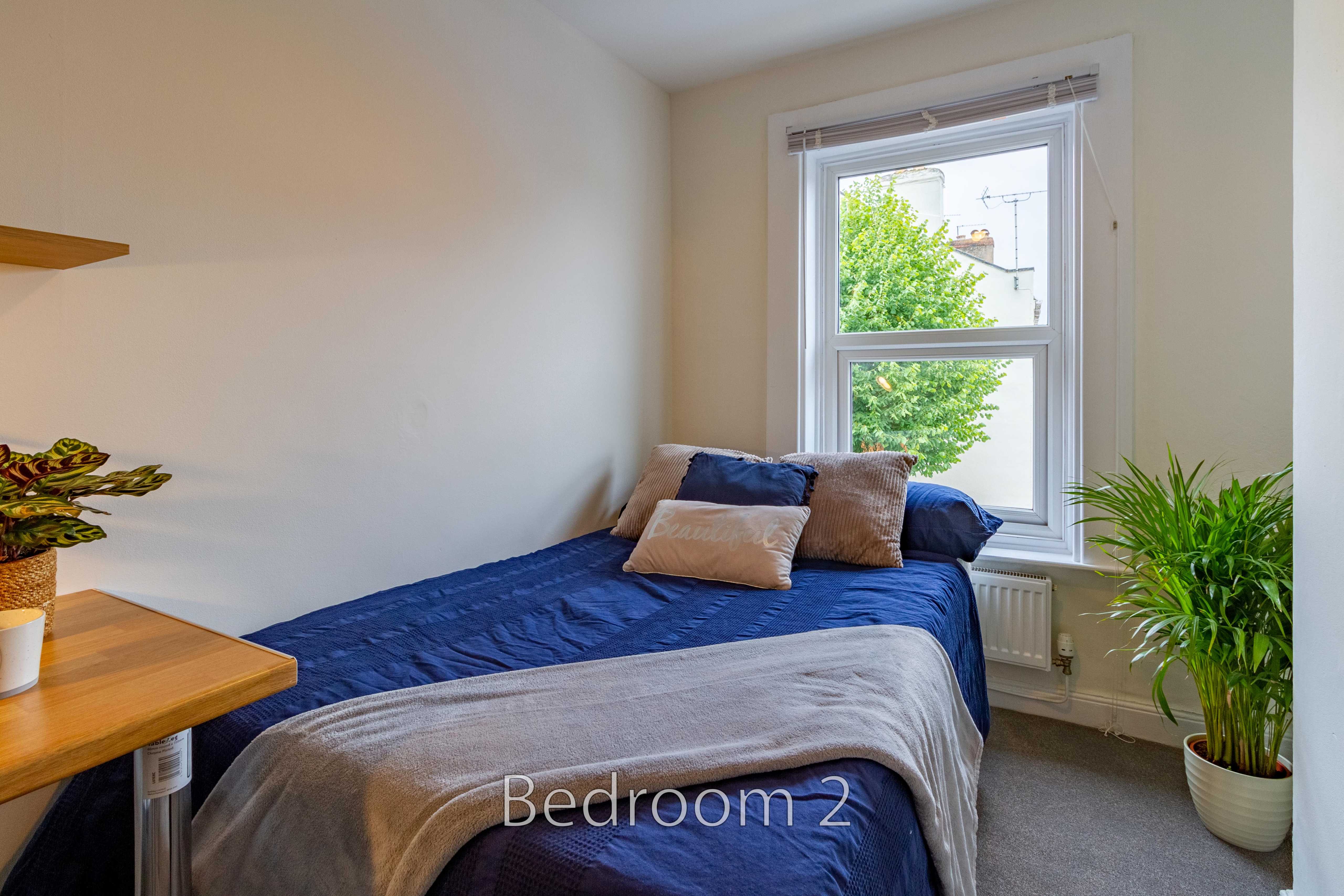 A small bedroom with a bed, window, radiator and potted plants.