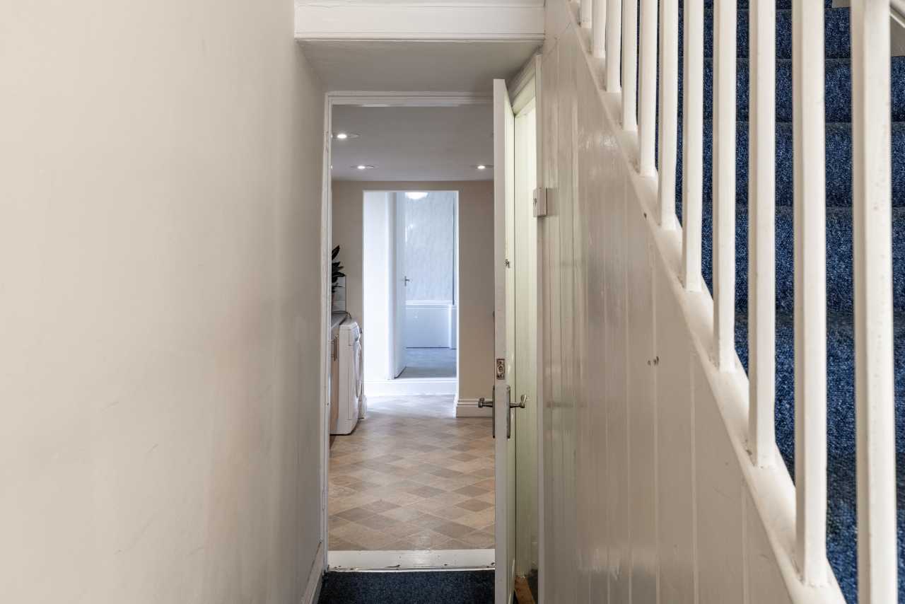 A narrow hallway with an open door, stairs, and a brighter room visible at the far end.