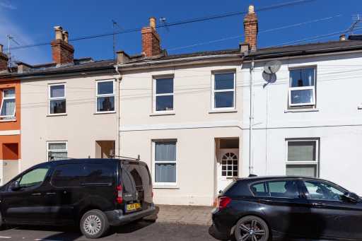 Street view of attached terraced houses with white façades, windows, doors, chimneys and parked cars.