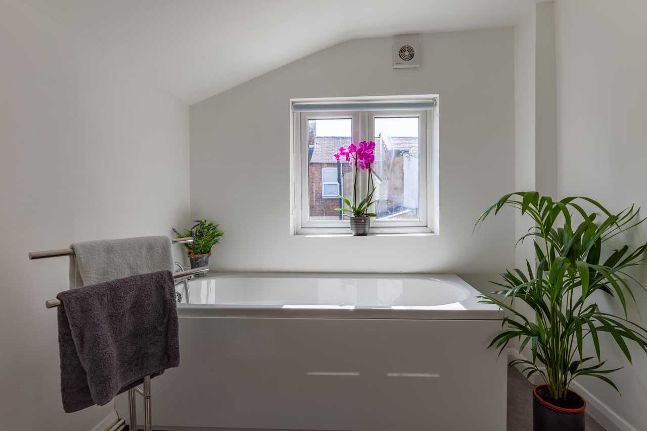 Bright bathroom with a white bathtub, window, towel rack, and potted plants.
