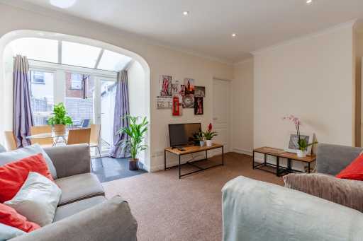 Bright living room with sofas, coffee tables, a television, plants and a large arched window.