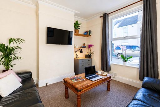 A furnished living room with two sofas, a television, coffee table, desk, shelves and a large window.