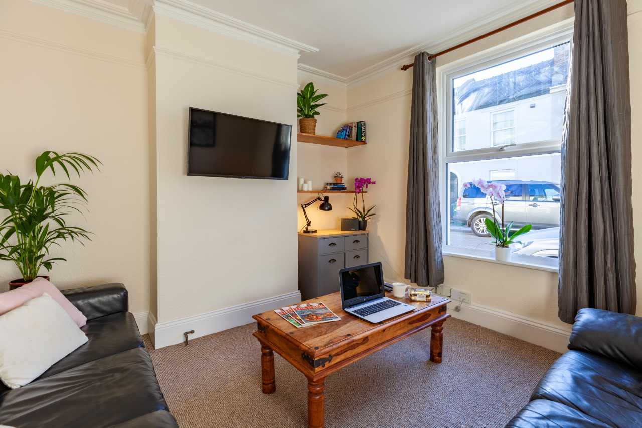 A furnished living room with two sofas, a television, coffee table, desk, shelves and a large window.