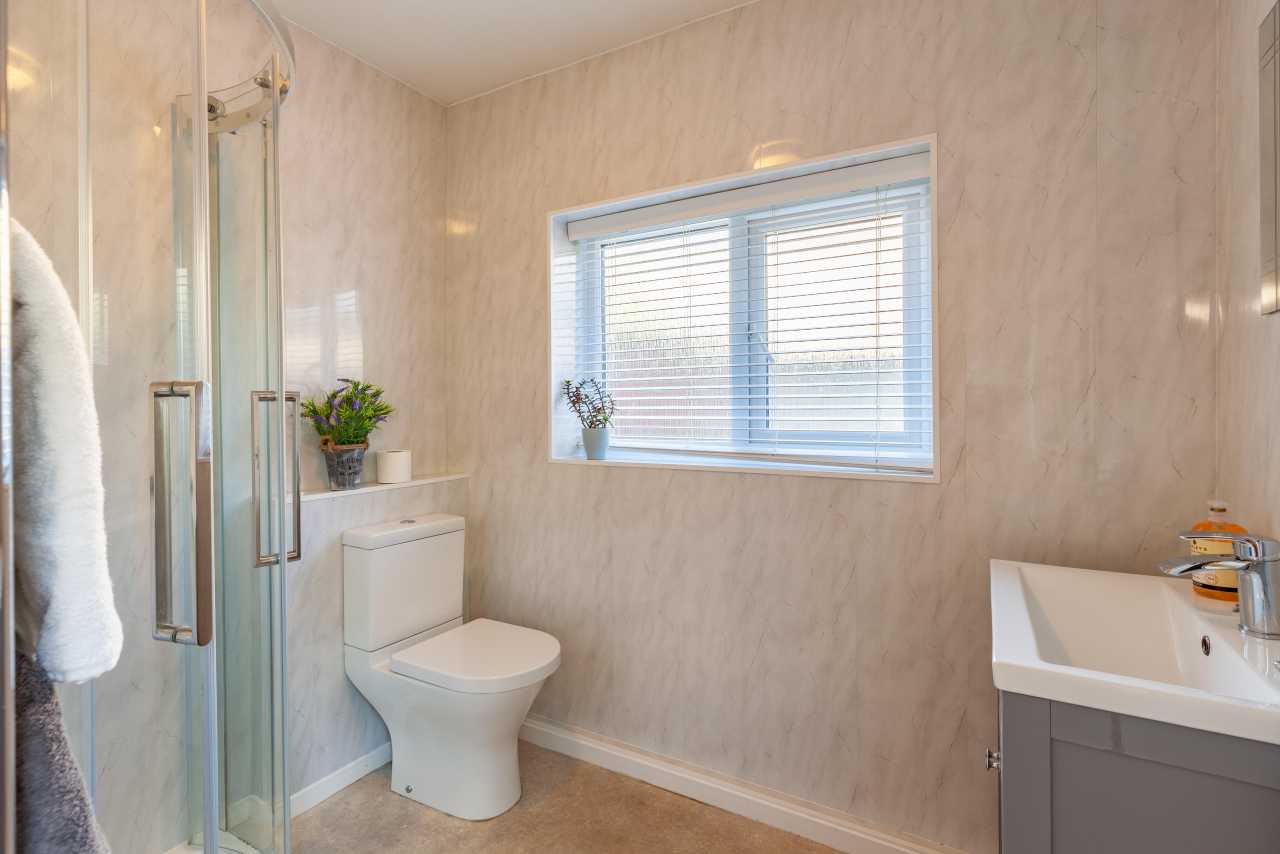 A bright bathroom with a glass shower enclosure, toilet, bathtub, vanity unit and window with blinds.