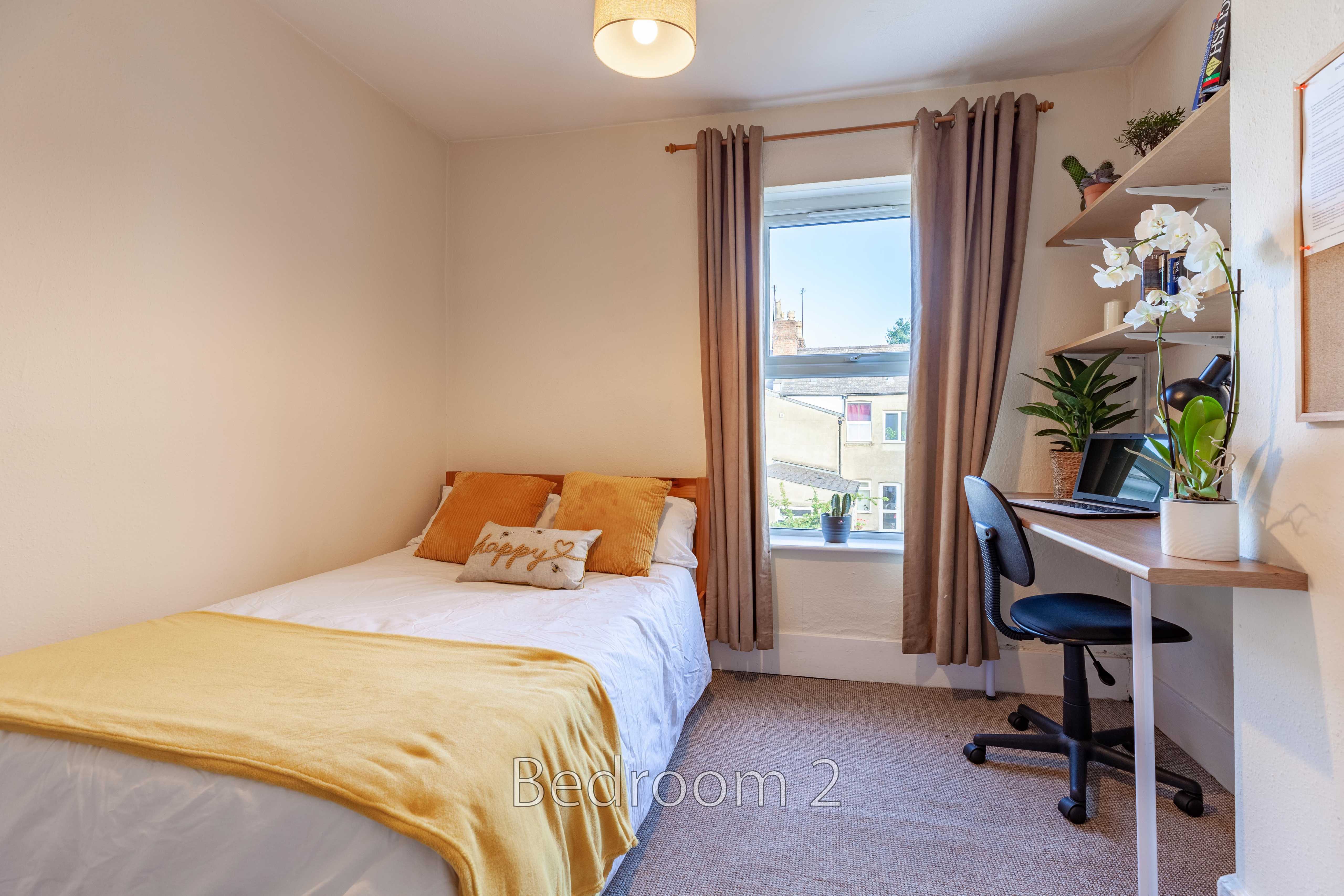 A bedroom with a single bed, window, curtains, desk and chair.