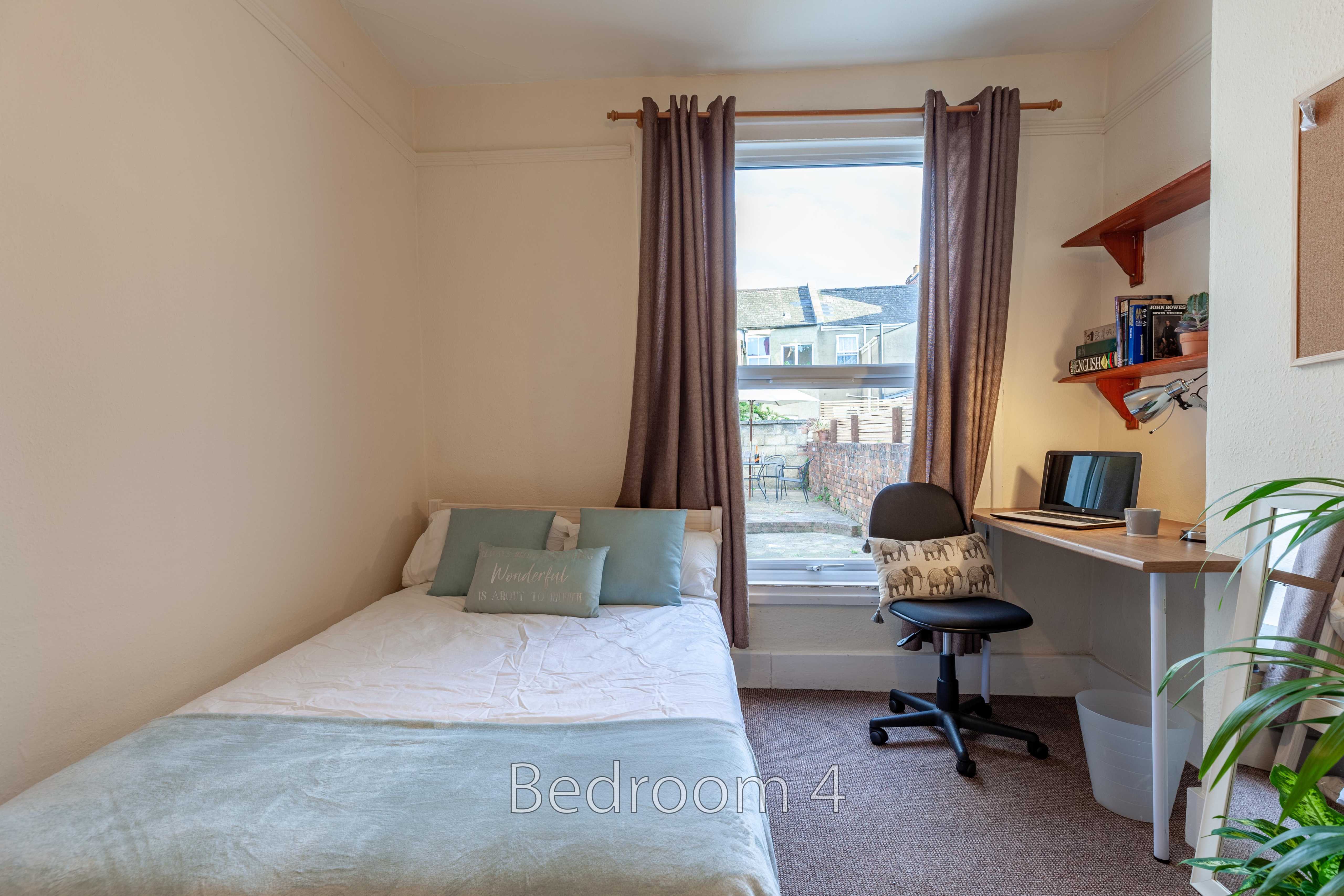 A bedroom with a single bed, desk, chair, shelving and a window.