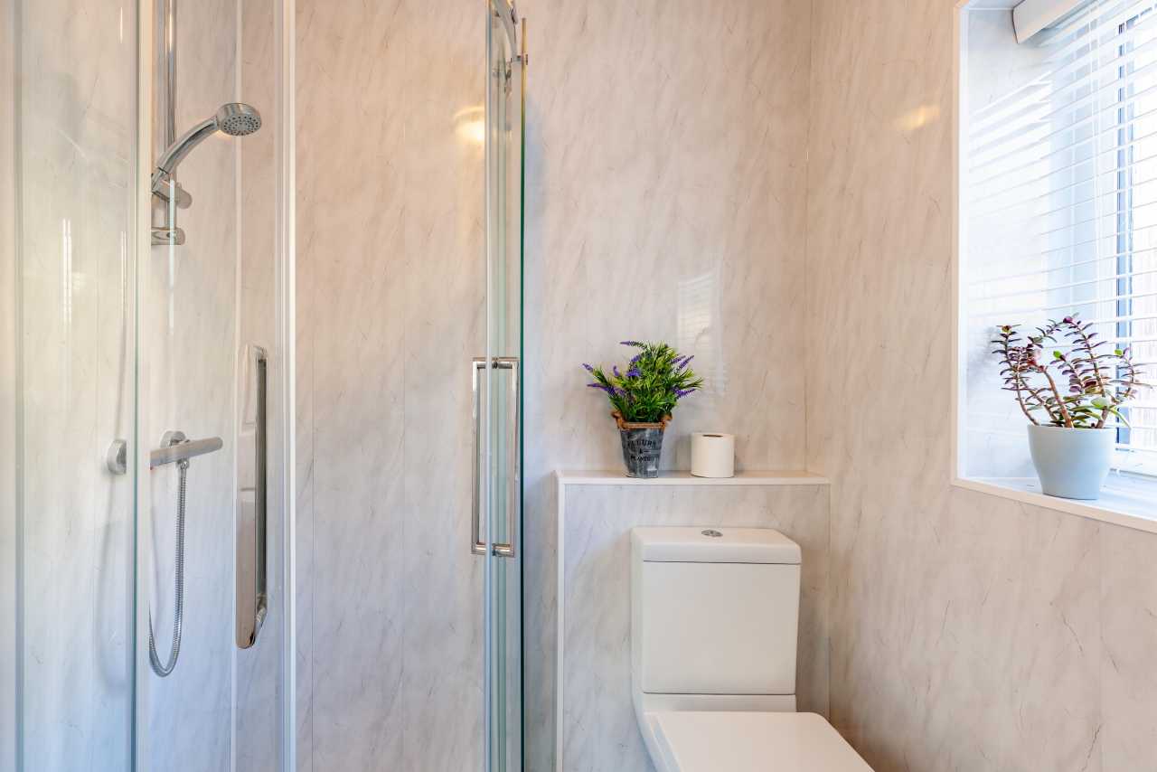 Bright bathroom with a glass-enclosed shower, toilet, window and potted plants.