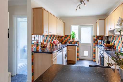 Bright fitted kitchen with wooden cabinets, colorful tiled backsplash, appliances, and a rear door.